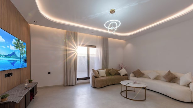 Una sala de estar moderna con un televisor de pantalla plana grande, un sofá, una mesa de centro y un mueble bajo de madera con objetos decorativos.