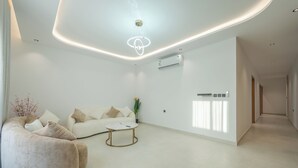 Una sala de estar moderna con un sofá blanco, un sillón informal, una mesa de centro y una lámpara en el techo.