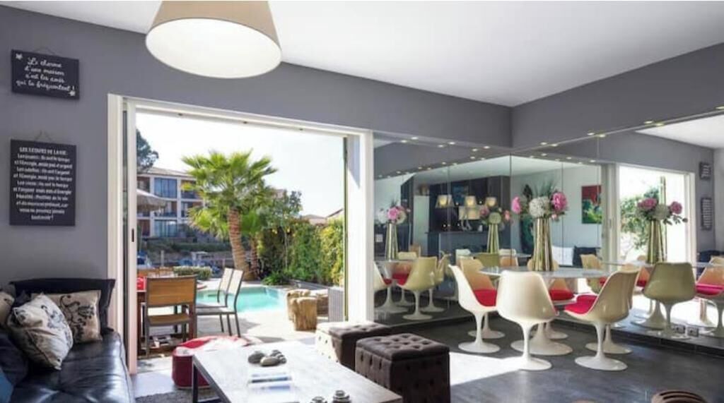 Ein modernes Wohnzimmer mit Blick auf einen Pool, ein Essbereich mit Stühlen und ein großer Spiegel, der den Raum reflektiert.