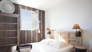 Een slaapkamer met een bed, een raam, een hoofdeinde met een lamp en een wandlamp.