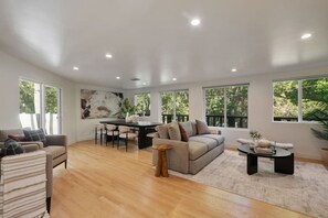 A spacious living room with a sofa, dining table, and chairs, large windows, and a ceiling with recessed lighting. - World Cup! Luxury Hollywood Retreat w/ Pool Table (West Hollywood)