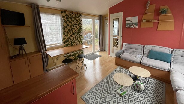 A cozy living area with a sofa, a small table, a TV, and a window with curtains. - Mobile Home for 4–6 Guests – 5 Minutes from the Beach, Châtelaillon-Plage (Châtelaillon-Plage)