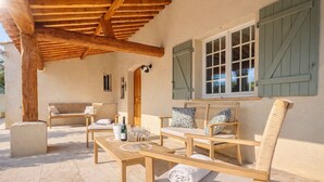 Eine Terrasse im Freien mit Holzmöbeln, einem Tisch mit Gläsern und einer Flasche sowie einer überdachten Sitzgelegenheit.