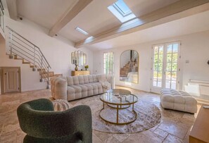 A spacious living room with a large sectional sofa, a round coffee table, and a staircase leading to an upper level. - VILLA PETIT MAS WITH PRIVATE POOL (Le Plan-de-la-Tour)