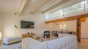 Ein modernes Wohnzimmer mit einer großzügigen Eckcouch, einem Flachbildfernseher und einem Essbereich mit Holzbalkendecke.