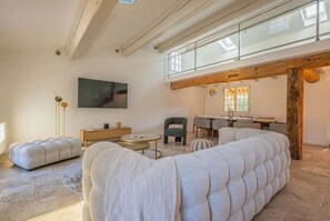 A modern living room with a large sectional sofa, a flat-screen TV, and a dining area with a wooden beam ceiling. - VILLA PETIT MAS WITH PRIVATE POOL (Le Plan-de-la-Tour)