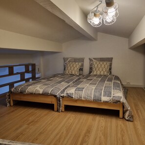 Un dormitorio con cama de madera, ropa de cama estampada, techo inclinado y lámpara colgante.