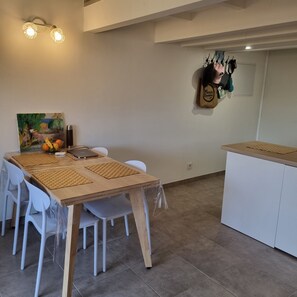 Un comedor con una mesa de madera, sillas blancas, un cuadro y un perchero en la pared.