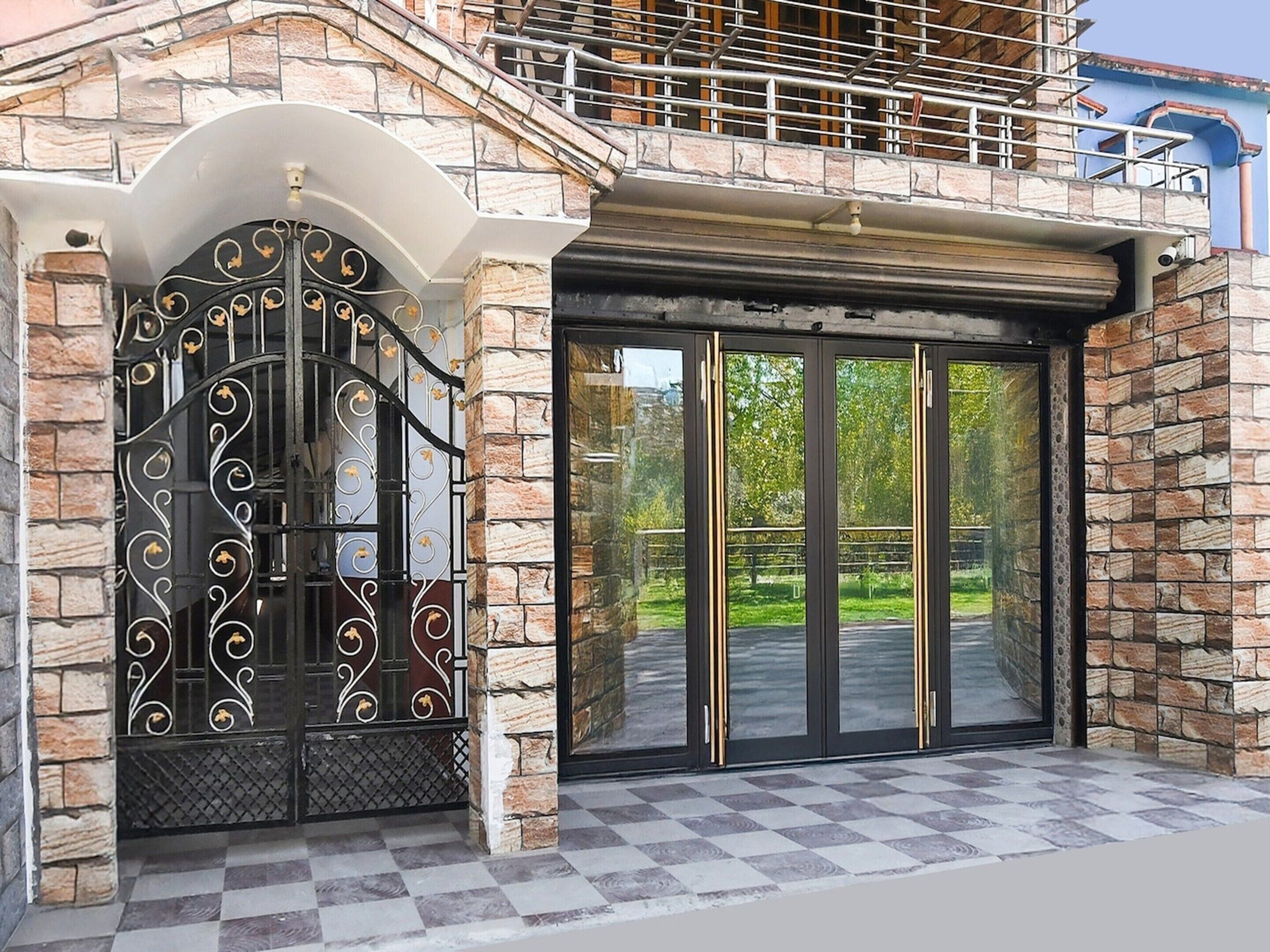 Een gevel met een decoratieve metalen poort, een glazen deur en een stenen gevel.