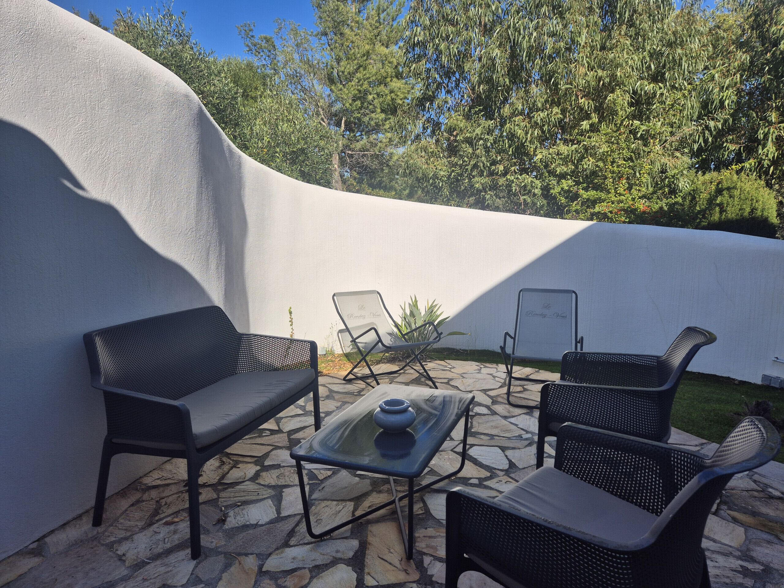 An outdoor patio with a stone floor, black wicker furniture, and a white wall.