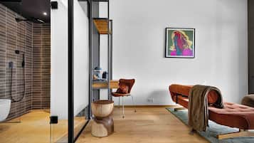 A modern interior with a wooden floor, a glass partition, a brown leather sofa, a wooden coffee table, and a colorful painting on the wall.