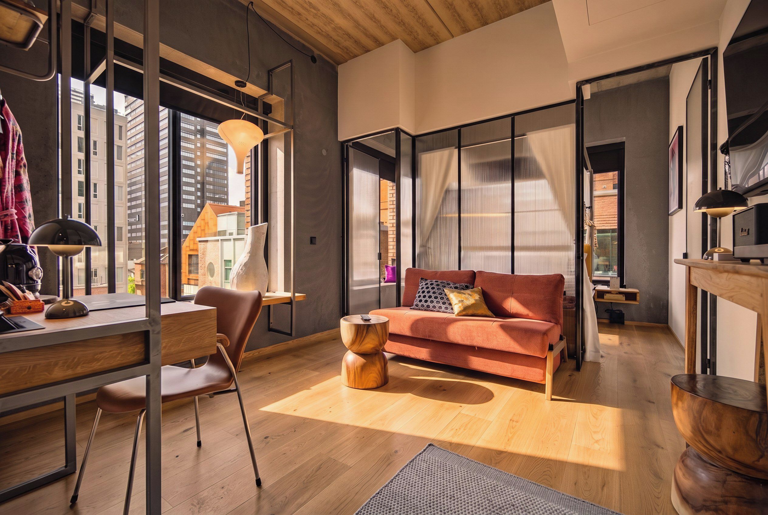 En moderne stue med en sofa, et skrivebord og en stol. Et stort vindue giver udsigt over byen.