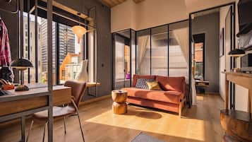 En moderne stue med en sofa, et skrivebord og en stol. Et stort vindue giver udsigt over byen.