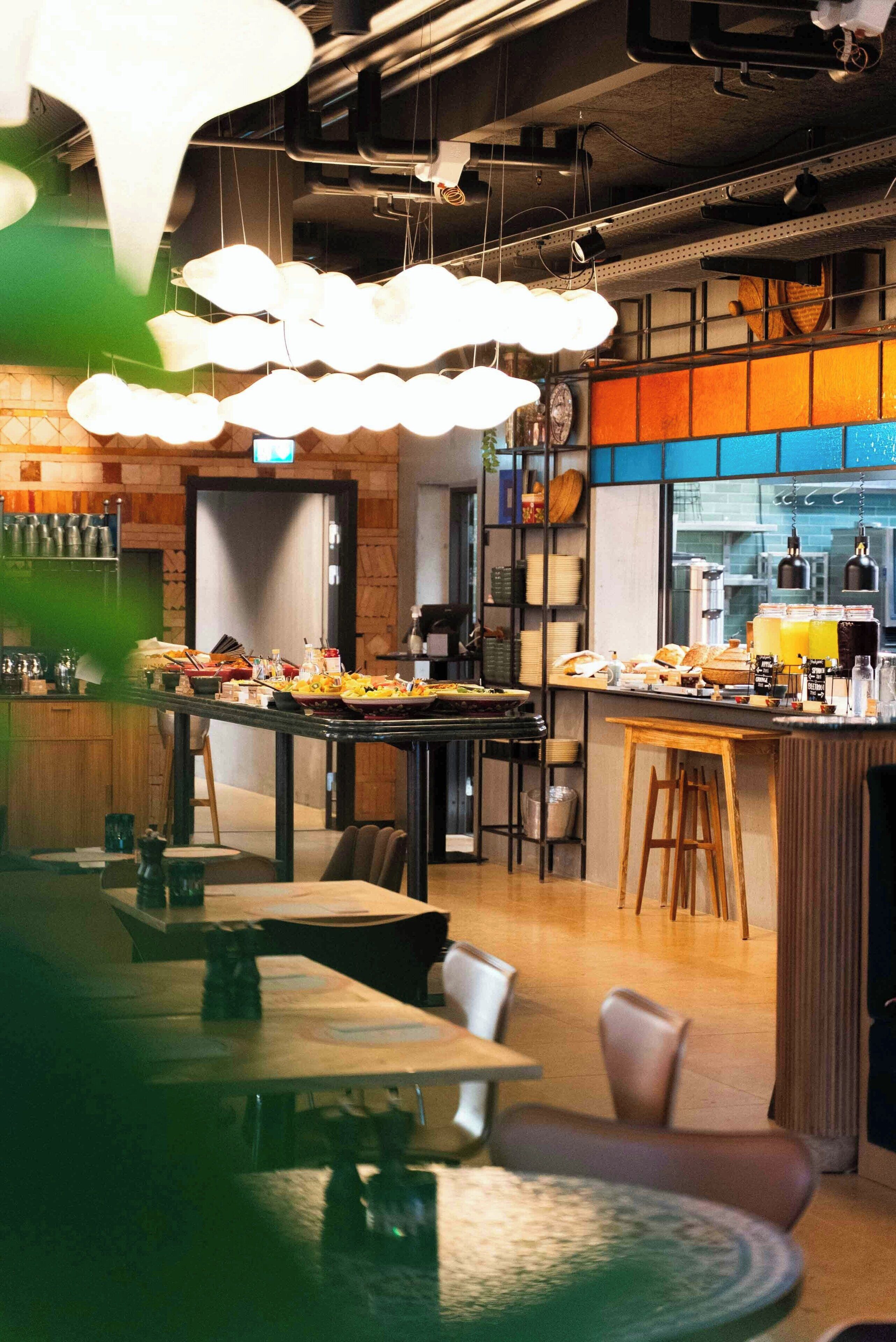 Et moderne restaurantmiljø med højt til loftet, synlige ventilationsrør og en bar.