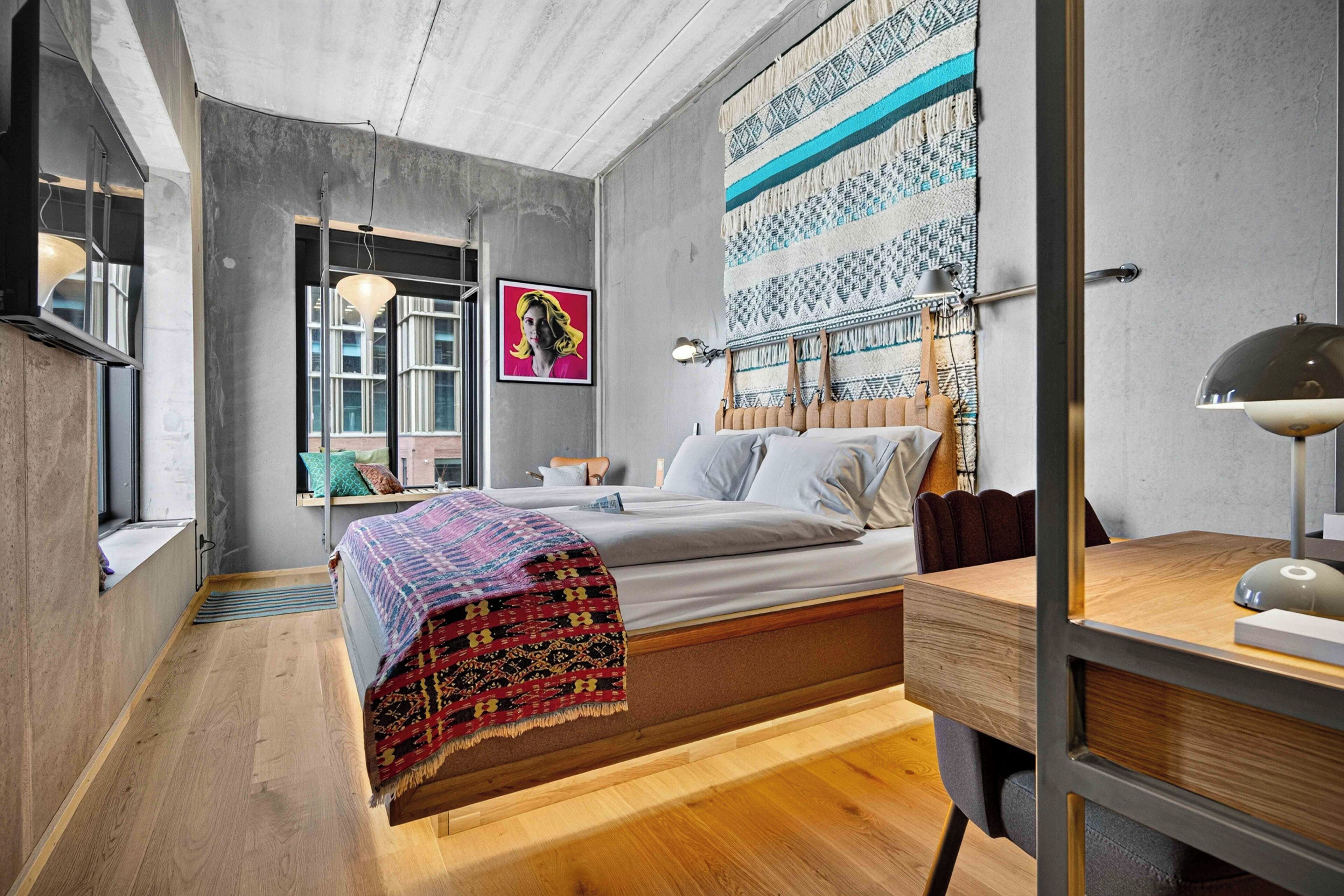 A modern bedroom with a bed, bedside table, lamp, and a large patterned tapestry on the wall.