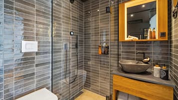 A modern bathroom with a glass-enclosed shower, a wooden vanity with a stone sink, and a mirror with toiletries.