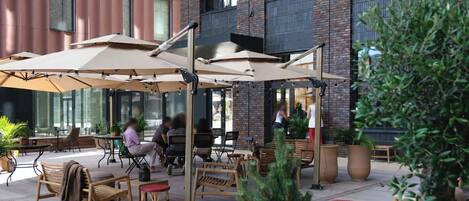Een terras met tafels, stoelen, parasols en plantenpotten.