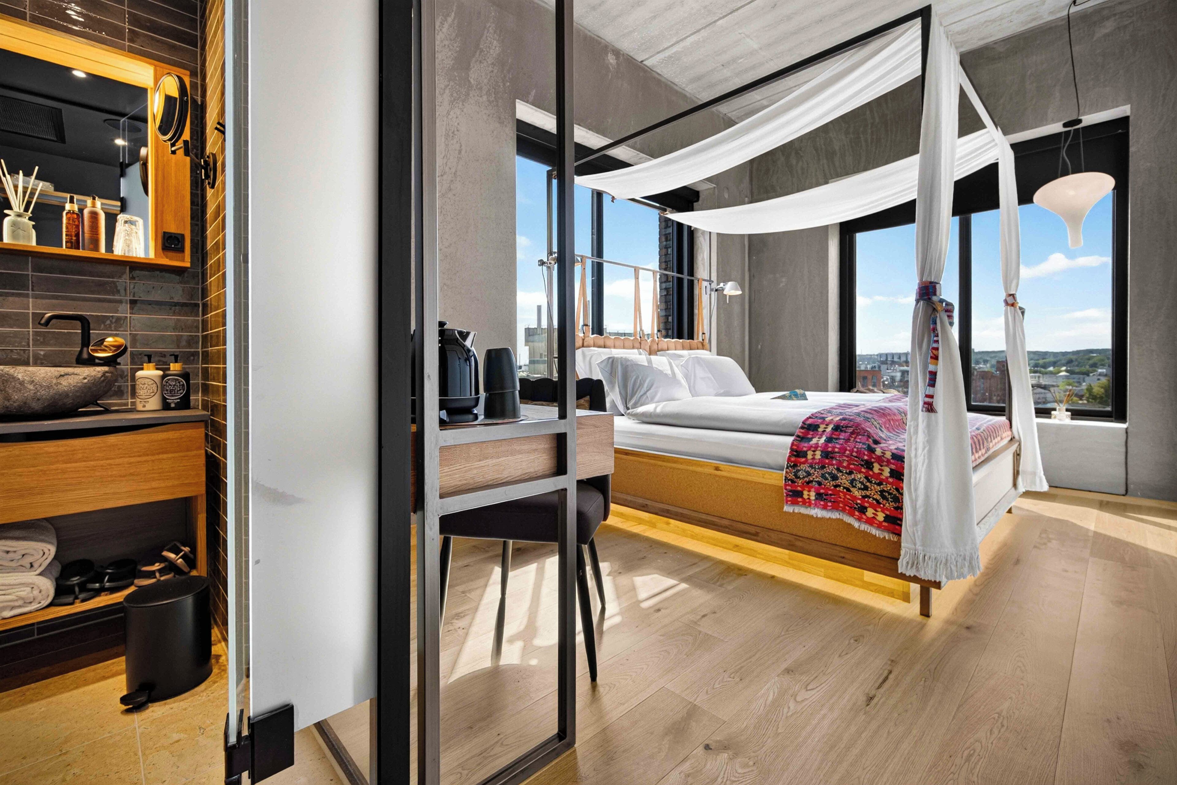 Ein modernes Schlafzimmer mit einem Himmelsbett, einer Holzablage mit Pflegeprodukten und Blick auf die Stadt.