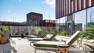 A rooftop terrace with lounge chairs, a small table, and potted plants.