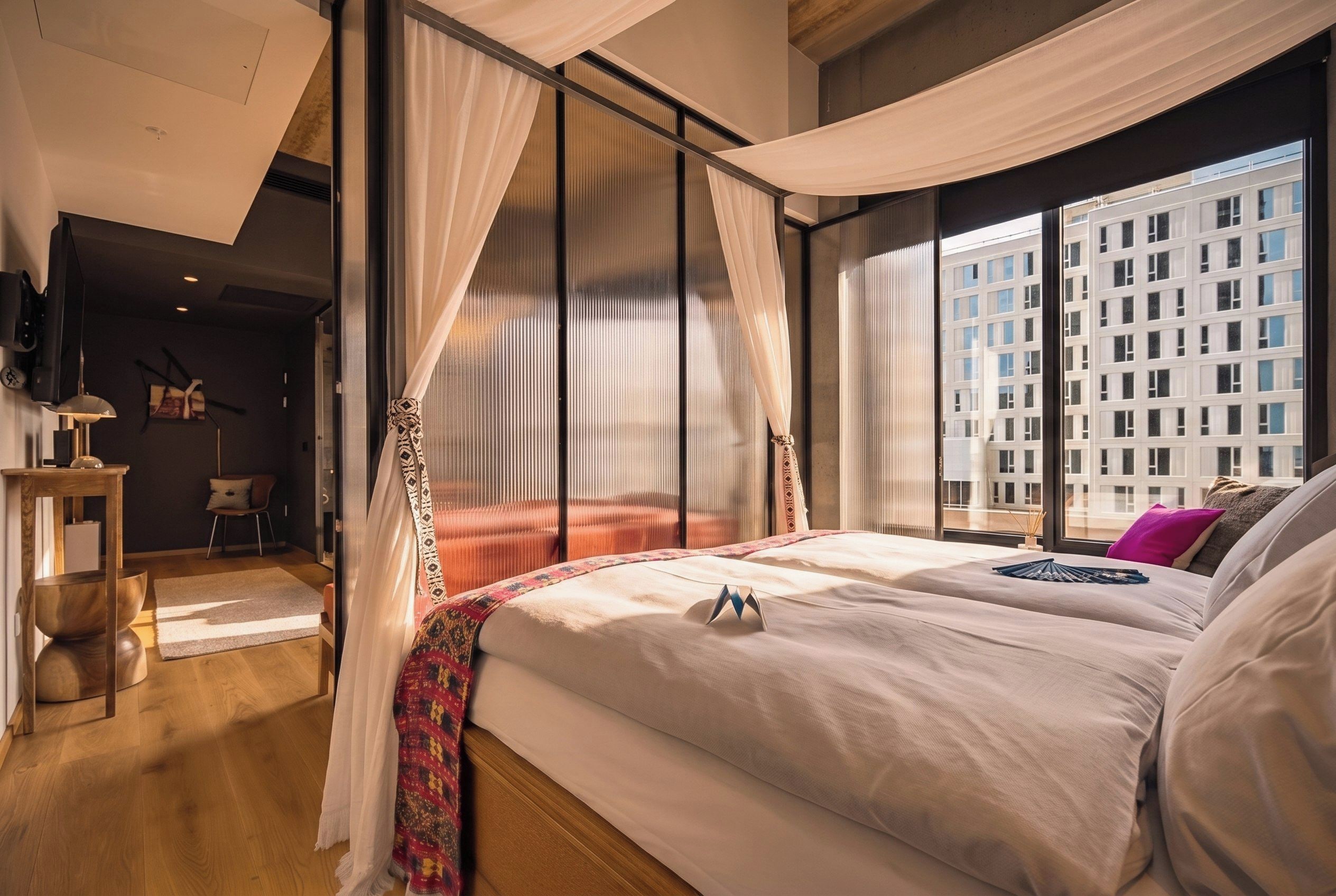A modern hotel room with a large bed, a view of the city, and a balcony.