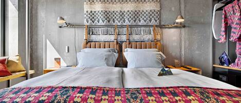 Un lit double avec une couvre-lit aux couleurs vives, une tête de lit ornée d’un motif tissé et deux lampes de chevet.