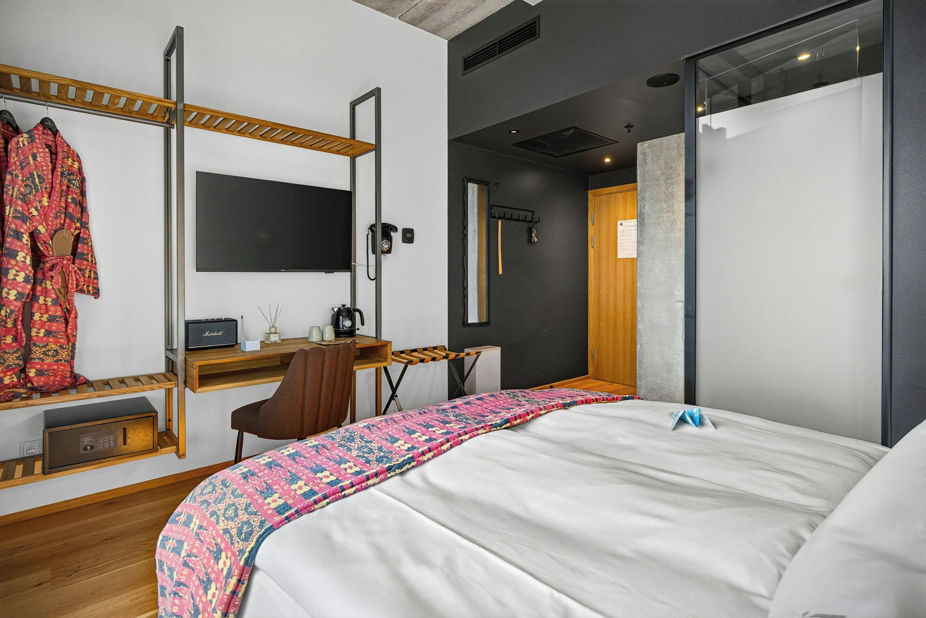 Una habitación de hotel moderna con cama, un escritorio con computadora, un espejo y un armario.