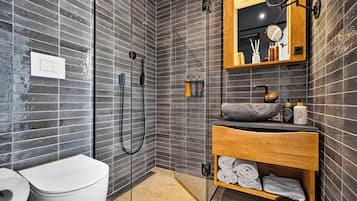 Un baño moderno con ducha, inodoro y tocador con espejo y artículos de aseo.