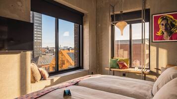 Un dormitorio moderno con un ventanal grande, una cama con almohadas, una lámpara colgante y vista a la ciudad.