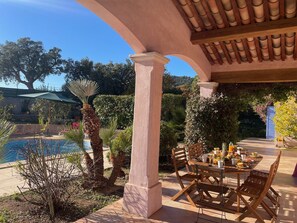 A patio with a pool, wooden chairs, and a table set for dining. - MAGNIFICENT VILLA LES CACTUS WITH PRIVATE POOL (Le Plan-de-la-Tour)
