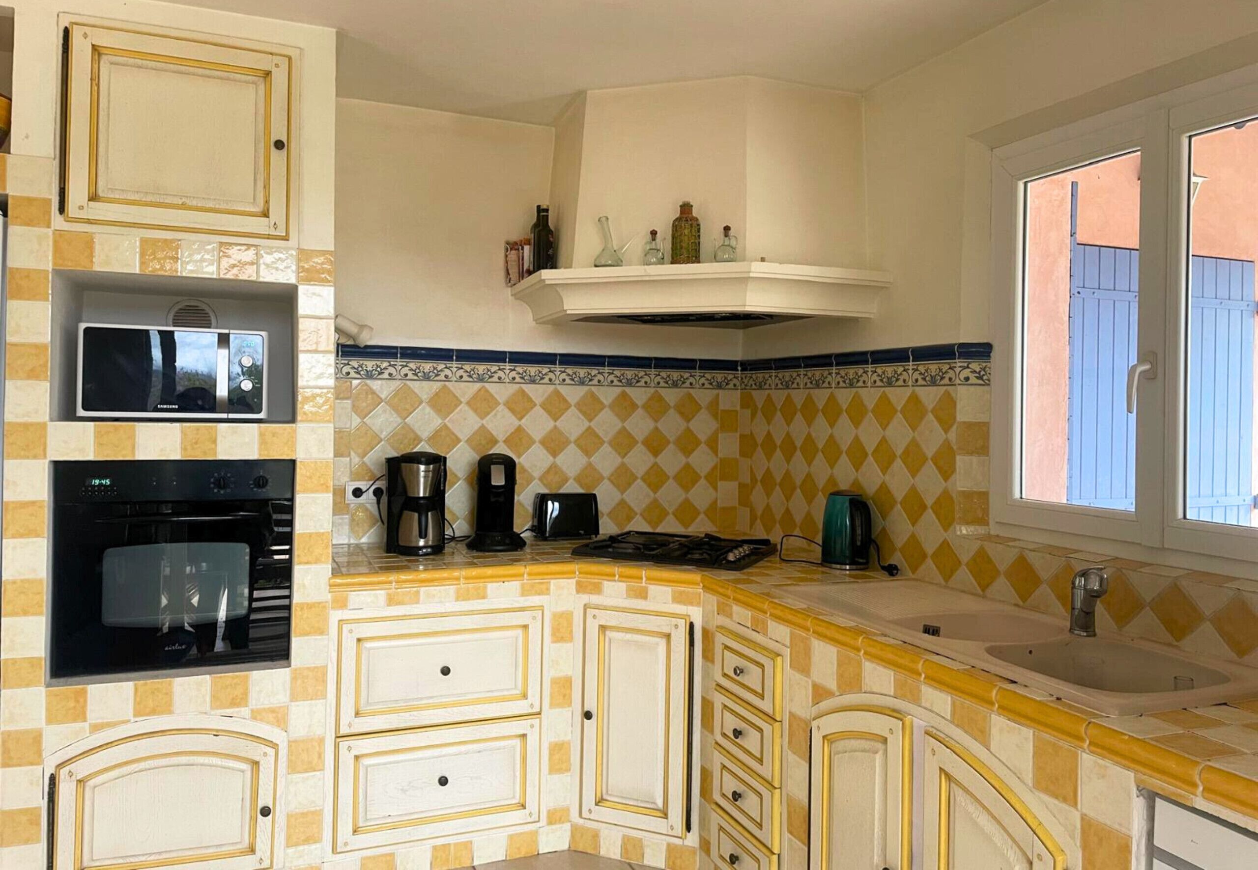 A kitchen with a microwave, oven, coffee maker, and a window with blue shutters.