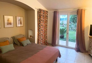 Ein Schlafzimmer mit Bett, Kissen, einem Nachttisch, einem Fernseher und einer Glastür zu einem Garten.