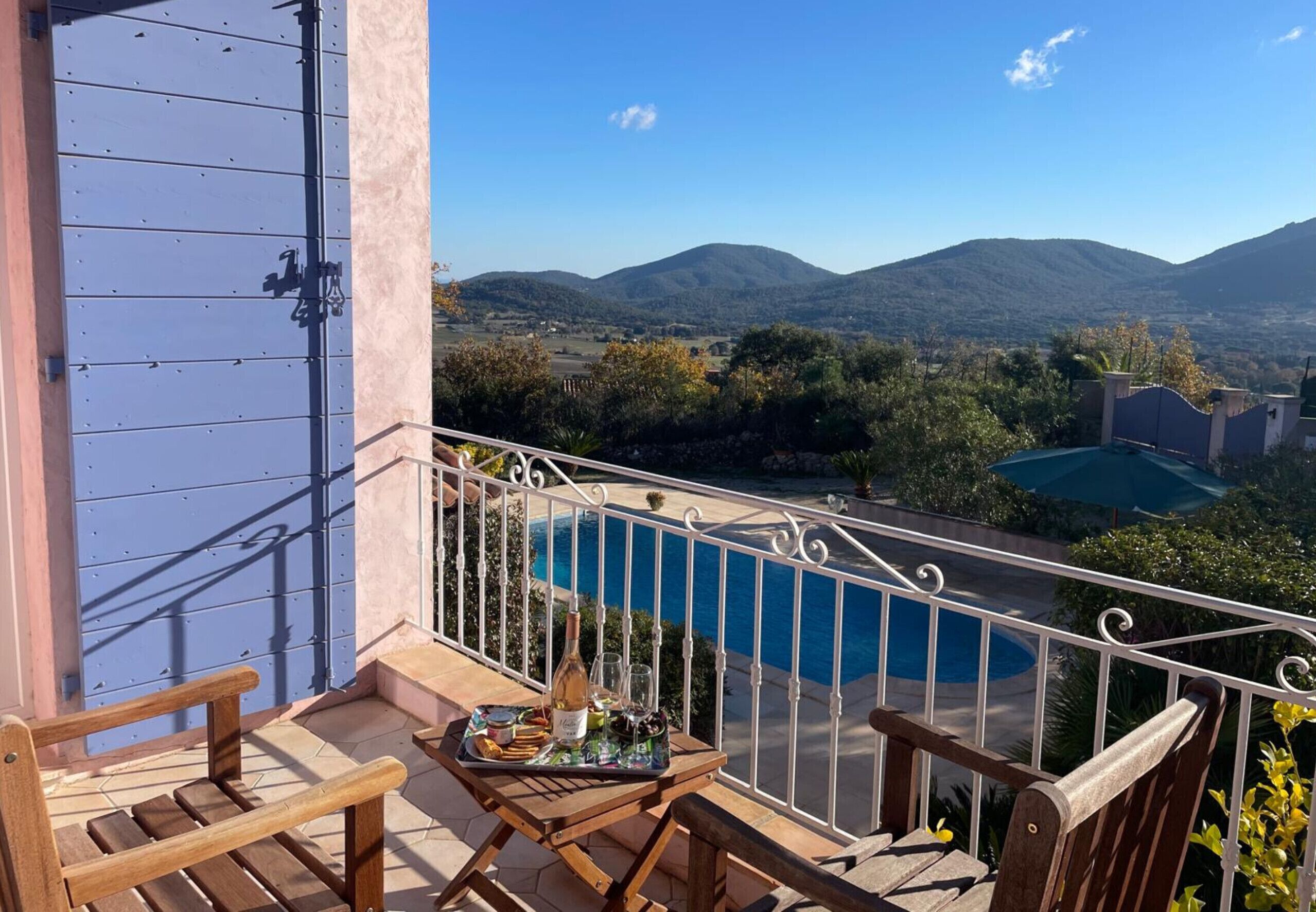 Een balkon met een zwembad, houten meubilair en een prachtig uitzicht op bergen.