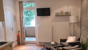 Ein Wohnzimmer mit einer Couch, einem Fernseher, einer Heizung und einem Fenster mit Vorhängen.