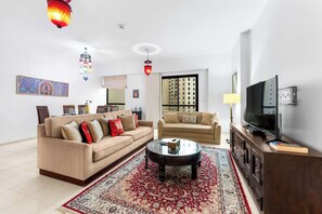 Ein Wohnzimmer mit zwei Sofas, einem Couchtisch, einem Fernseher und einem gemusterten Teppich.