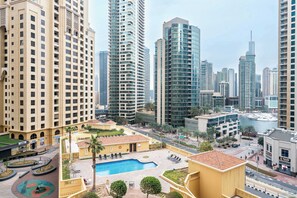 A high-rise hotel with a swimming pool, palm trees, and a marina in the background. - StayShort - Cozy & Modern 1BR in JBR Sleeps 4 (JBR)