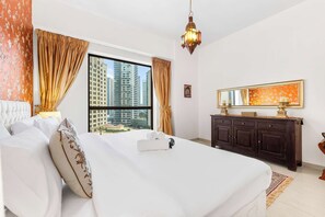 Ein Hotelzimmer mit einem großen Bett, Blick auf hohe Gebäude, einer dunklen Holzkommode und einer hängenden Leuchte.