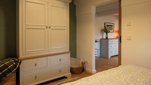 Une chambre avec une grande armoire blanche, un lit recouvert d’une couvre-lit à motifs et un panier en osier.