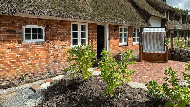 Une maison traditionnelle en briques, avec un toit de chaume, un banc en bois et un petit jardin.