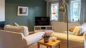 Un salon avec un canapé, un téléviseur, une lampe et une fenêtre avec des rideaux.