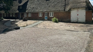 Un bâtiment avec un toit de chaume, une allée gravillonnée et une porte blanche.