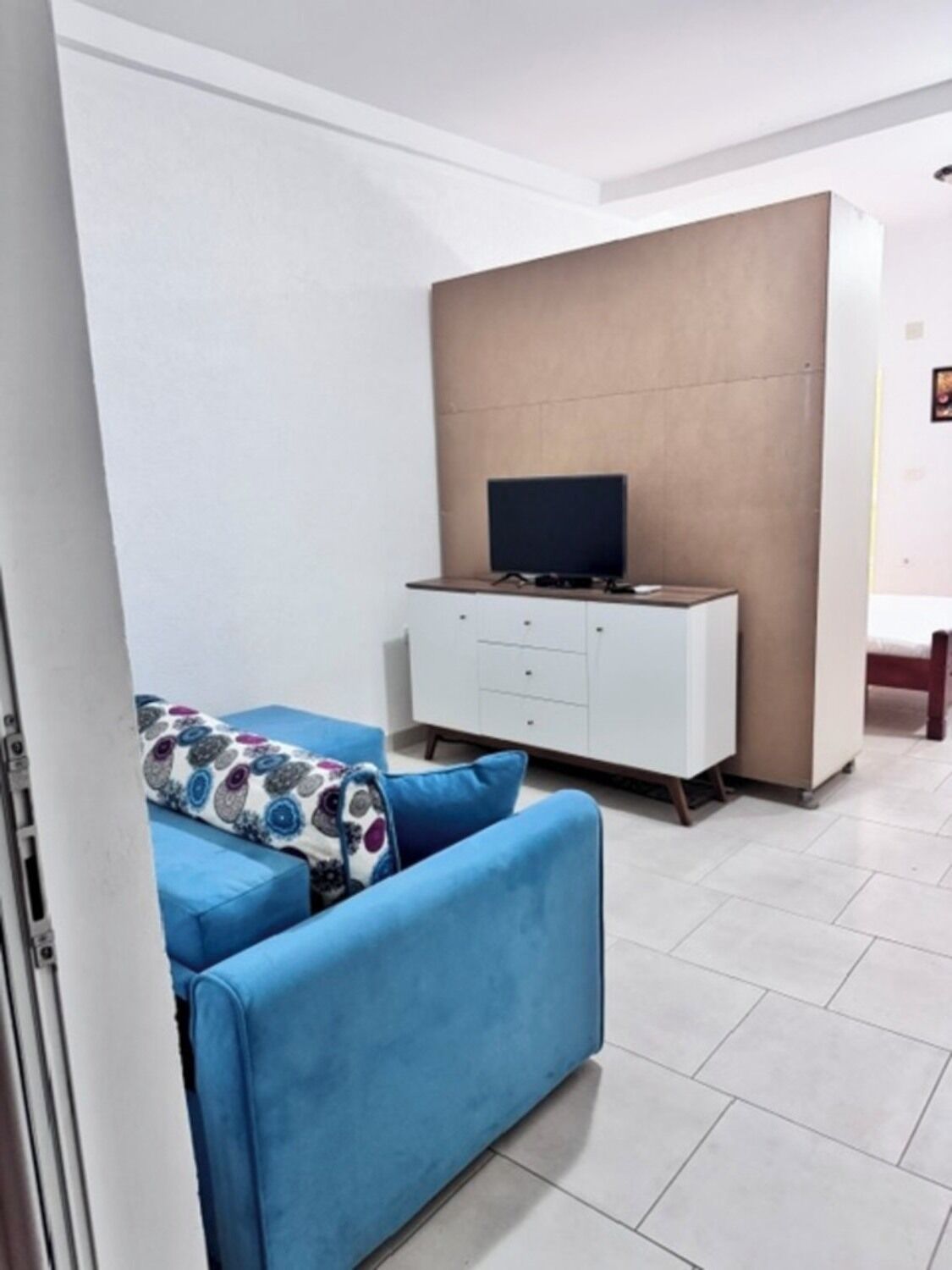 Ein Wohnzimmer mit einem blauen Sofa, einem weißen Schrank und einem Fernseher.
