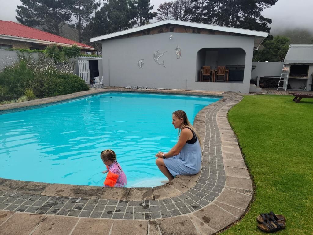 Une piscine bordée de carreaux, un patio couvert et un bâtiment avec un toit rouge en arrière-plan.