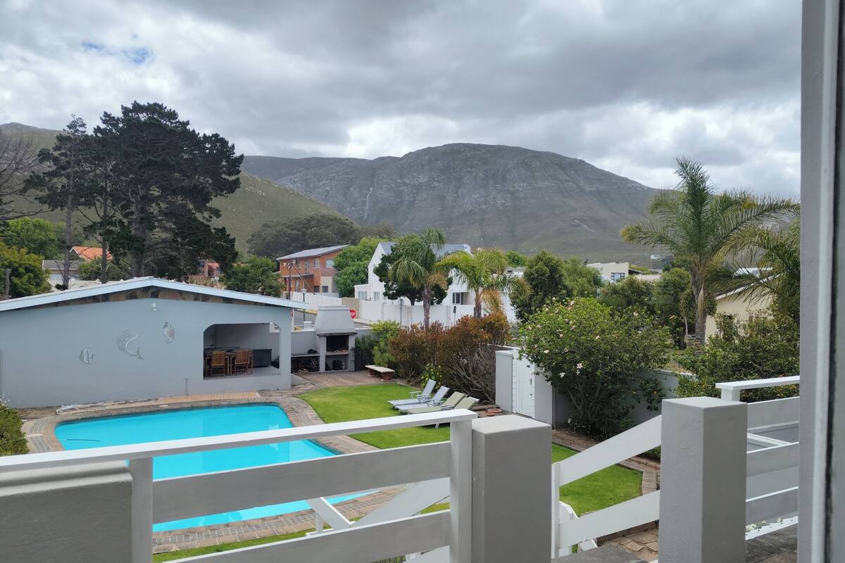 A pool area with a view of mountains, a barbecue area, and a white fence.