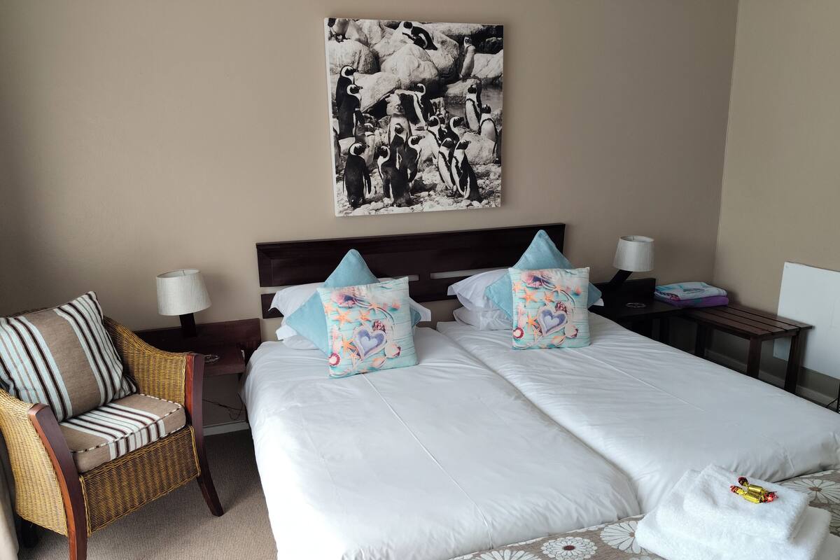 A hotel room with a bed, two pillows, a chair, a nightstand, a lamp, and a picture on the wall.