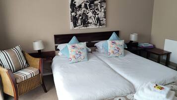 A hotel room with a bed, two pillows, a chair, a nightstand, a lamp, and a picture on the wall.