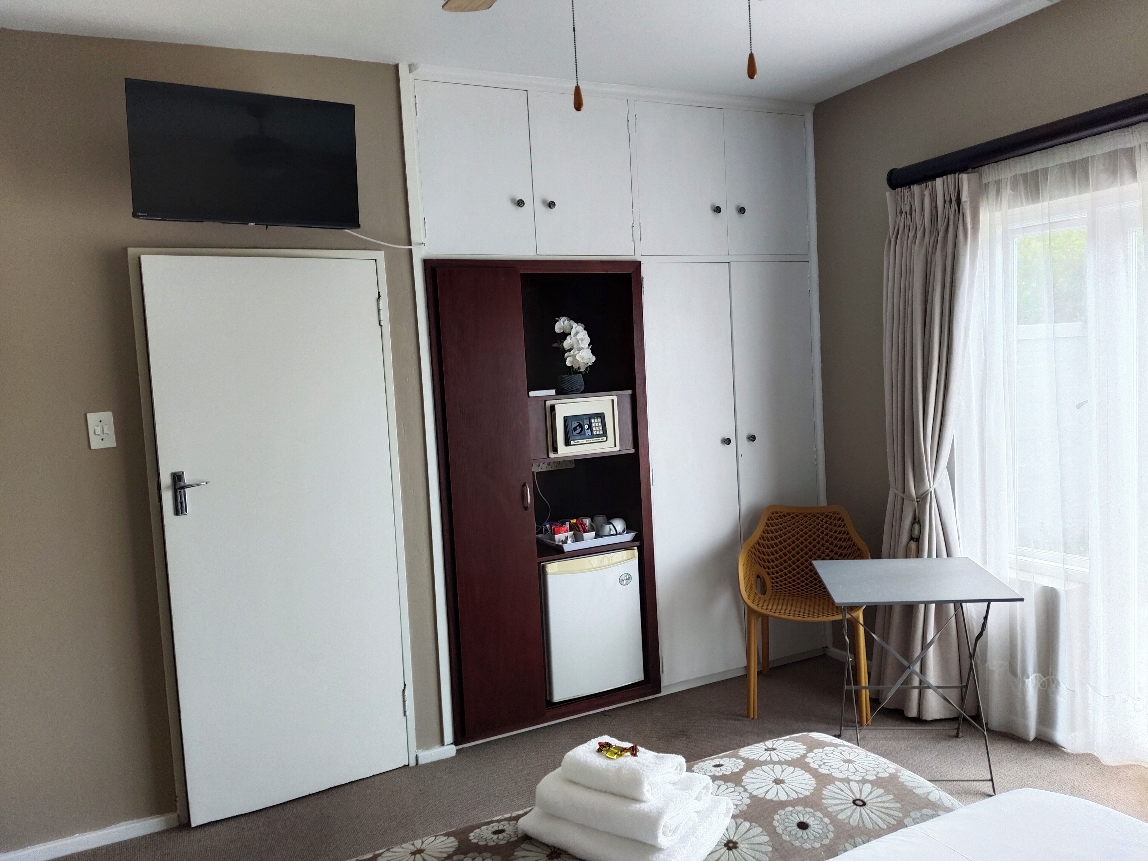 A bedroom with a wardrobe, a television, a desk, and a chair.