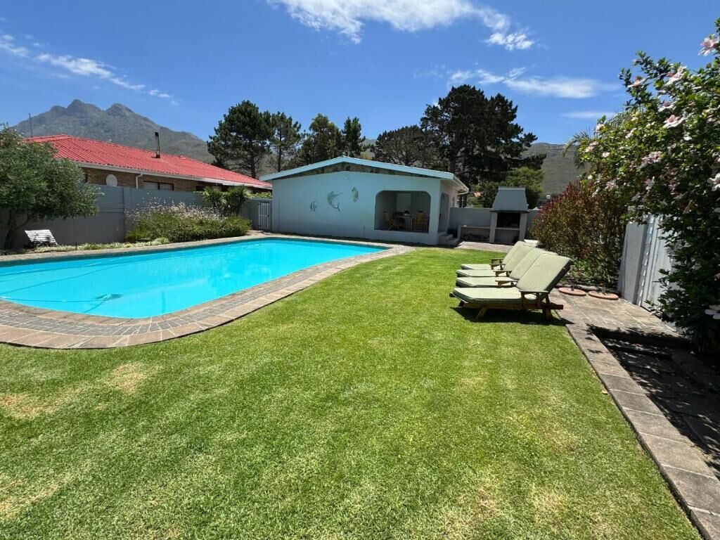 A swimming pool with a grassy area, lounge chairs, and a small building with a red roof.