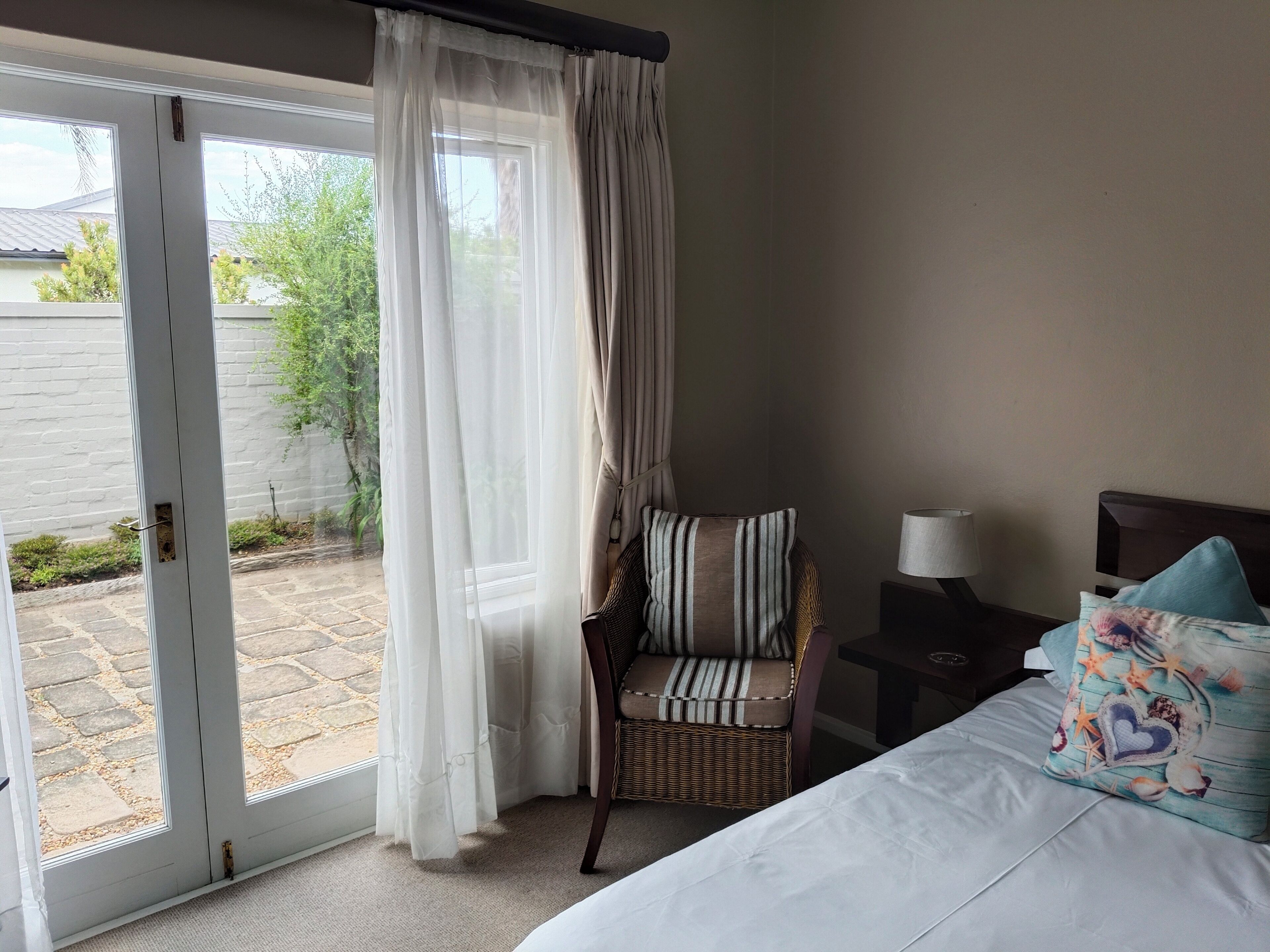 A hotel room with a bed, a chair, a nightstand, a lamp, and a sliding glass door to the outside.