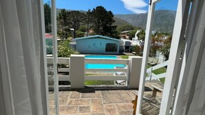 An outdoor patio area with a pool, stone flooring, and a view of a mountain and houses in the background. - Moments Guesthouse (Kleinmond)