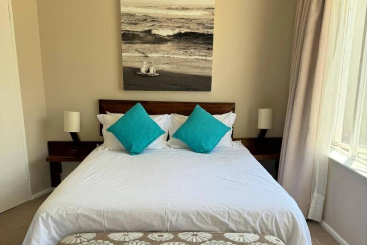 A hotel room with a bed, a painting of a beach scene, and a window with curtains.